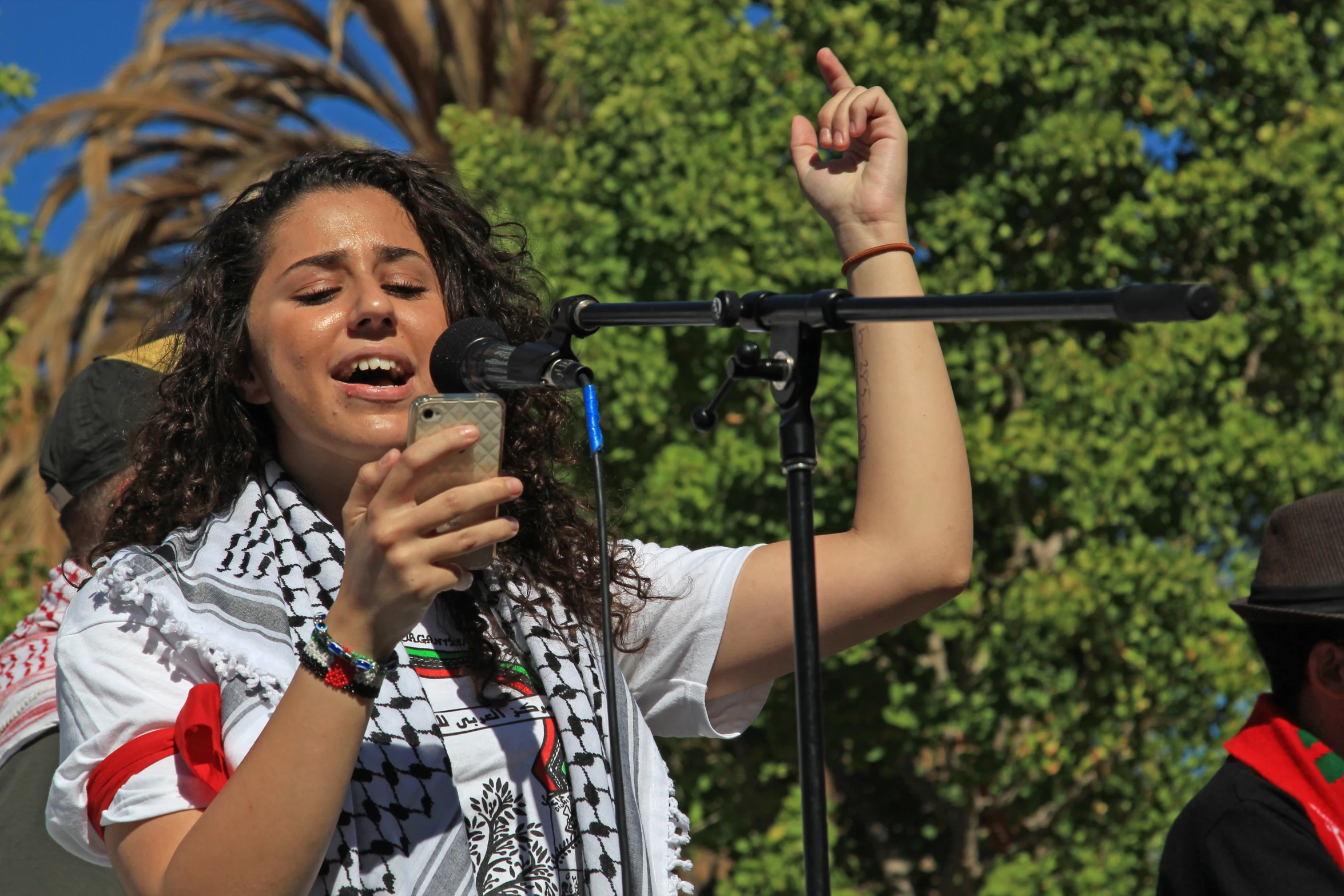 a woman in an ethnic dress smiles and holds up her phone to the microphone