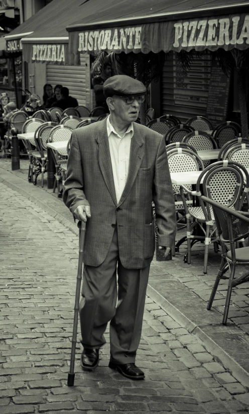 a man in a jacket and hat holding a cane walking down the street