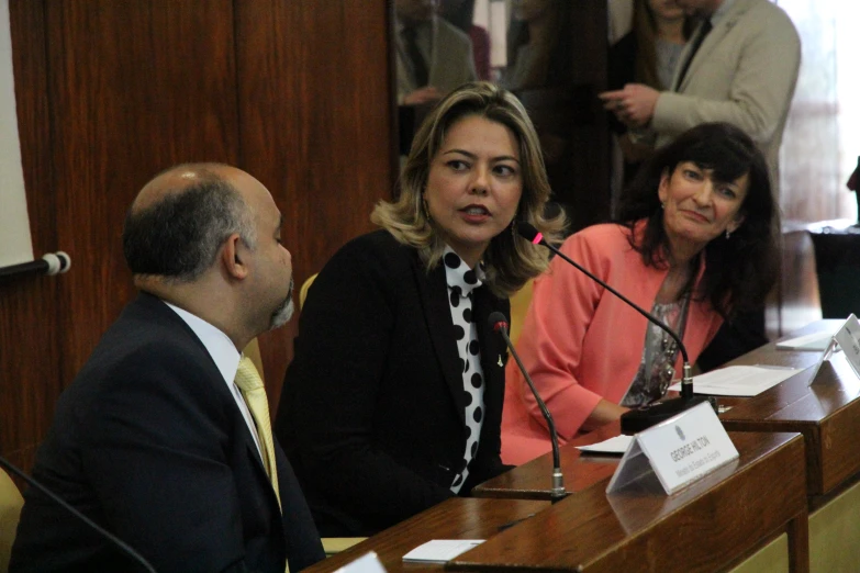 a woman speaking to two men in a wooden meeting room