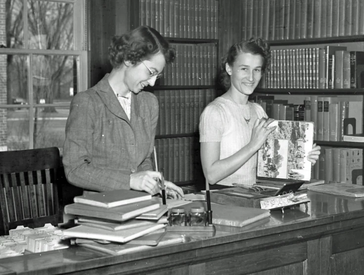 vintage black and white po of two women at bookcase looking at book