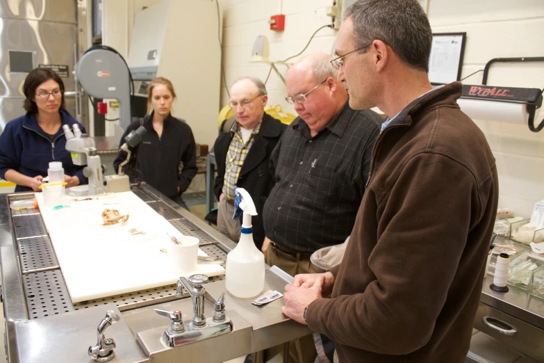 a group of people in a lab standing and watching soing on a table