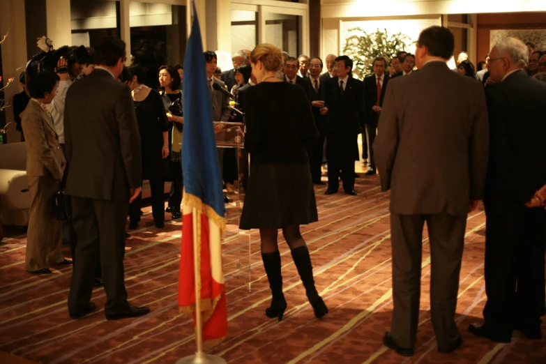 a crowd of people stand inside a building in front of a flag