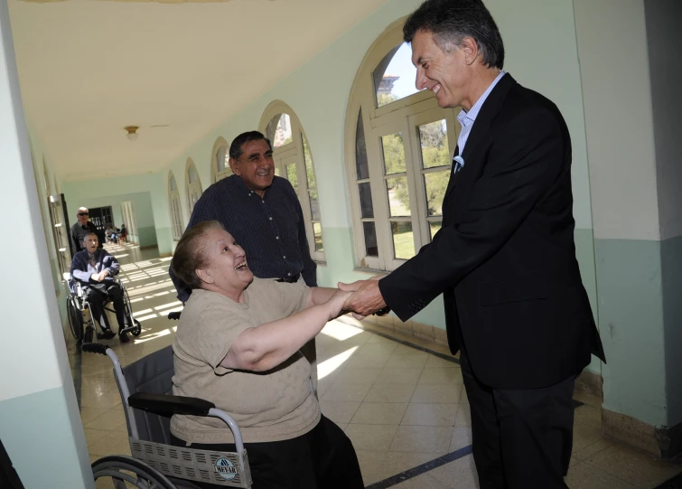 two people shake hands while in front of the door, with other people and three others