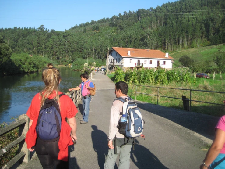 four people walking over a bridge near a house