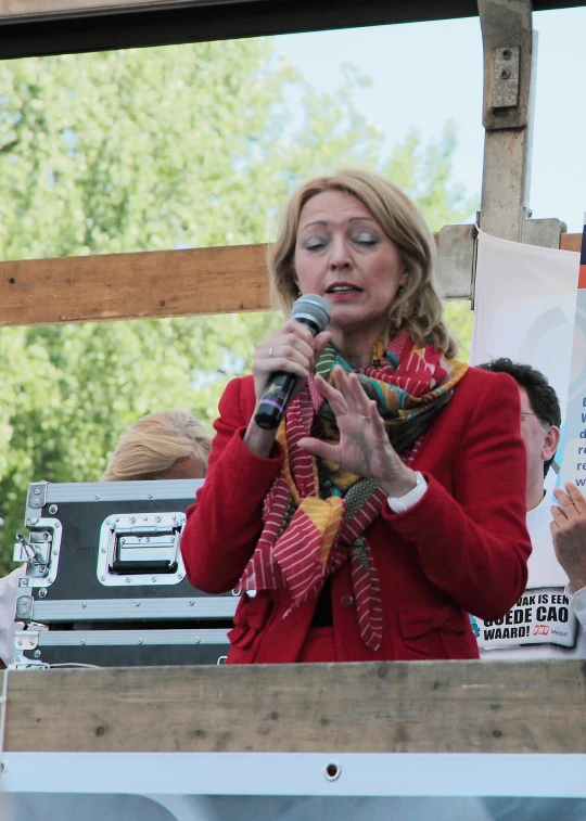 woman with red jacket speaking into a microphone