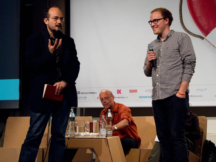 two men speak with each other on stage