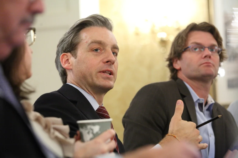 two men sit at a conference table and look to one side