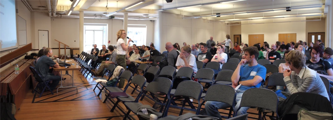 a group of people are sitting in the room and some stand up speakers