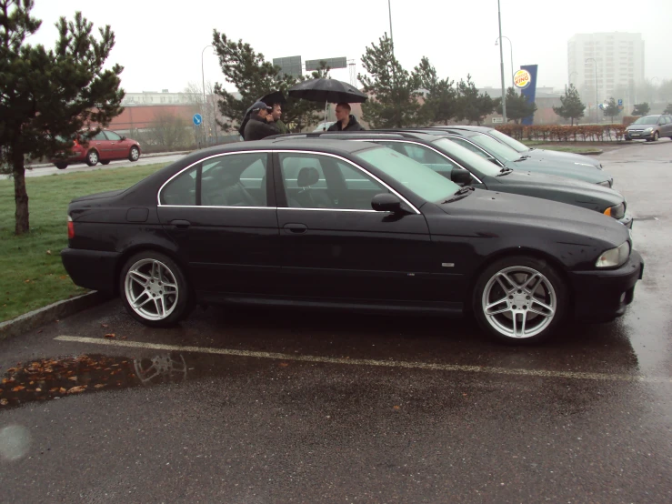 a black bmw parked in a lot with two people standing behind it