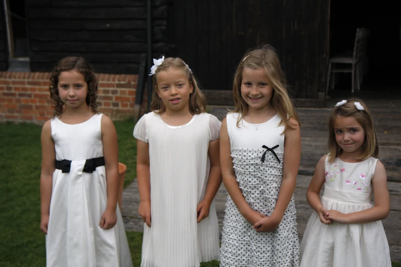 five girls wearing white dresses and standing together in front of a brick building