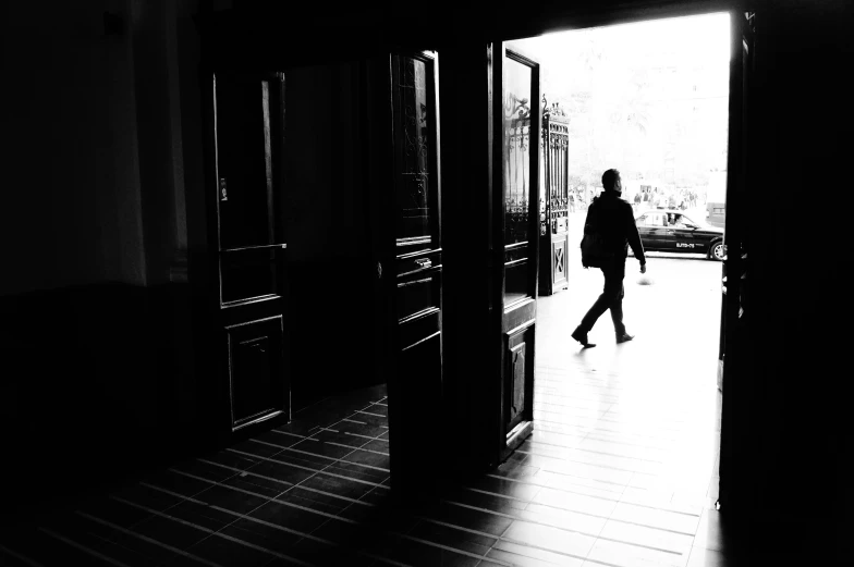 person walking through doorway of dark building with doors opened