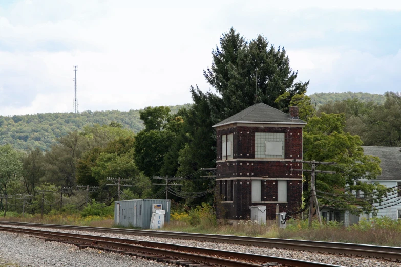 a lone brick building by railroad tracks with lots of trees