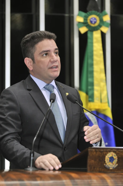 a man is speaking at a podium in front of flags