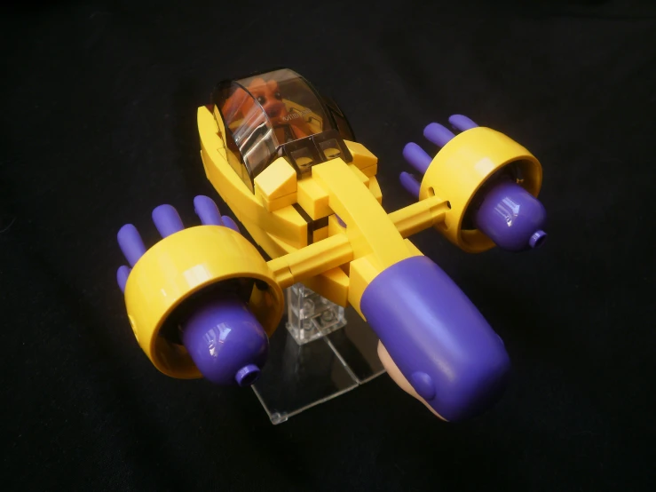 a yellow toy car with purple wheels on a clear stand