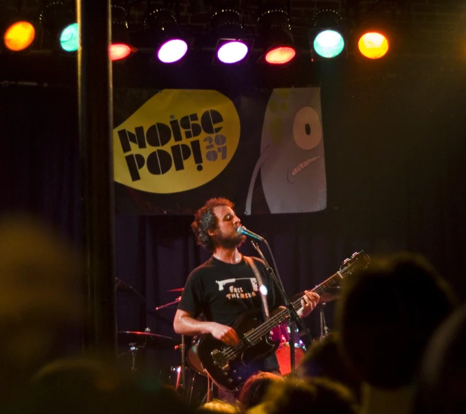 a man with black guitar on stage in front of a crowd