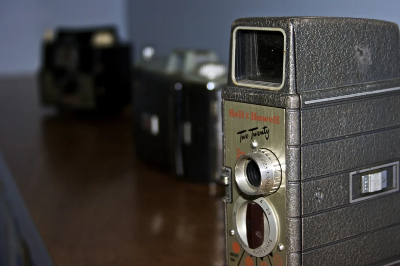 two old fashioned camera sitting on top of a wooden table