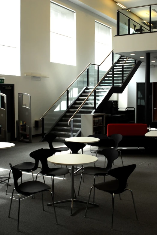 tables, chairs and stairs in a room with white walls