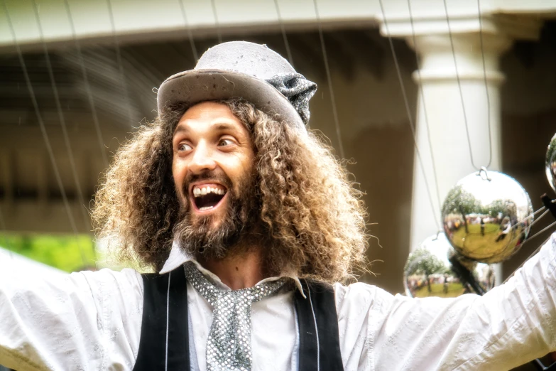 a bearded man with long hair wearing a hat and holding up some chrome balls