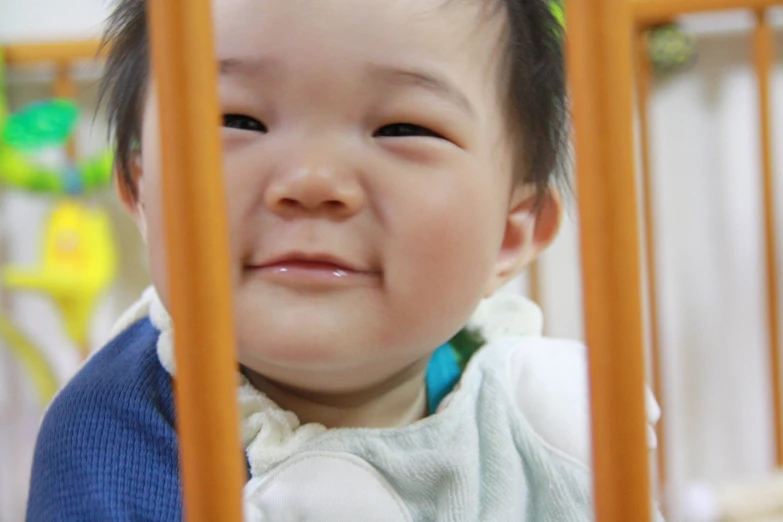 a little child sitting inside a orange baby crib smiling