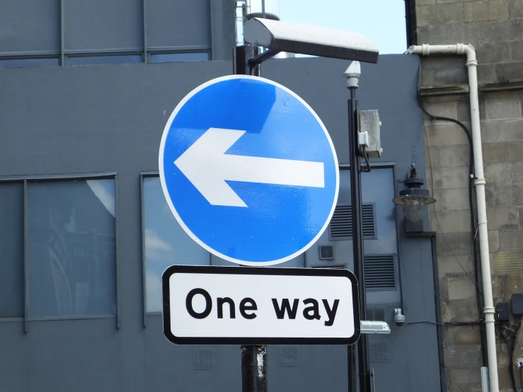 there is a blue one way sign hanging from a street pole