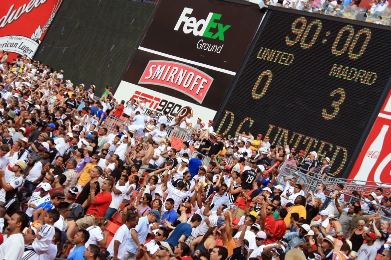 a crowd of people standing in front of a large score board