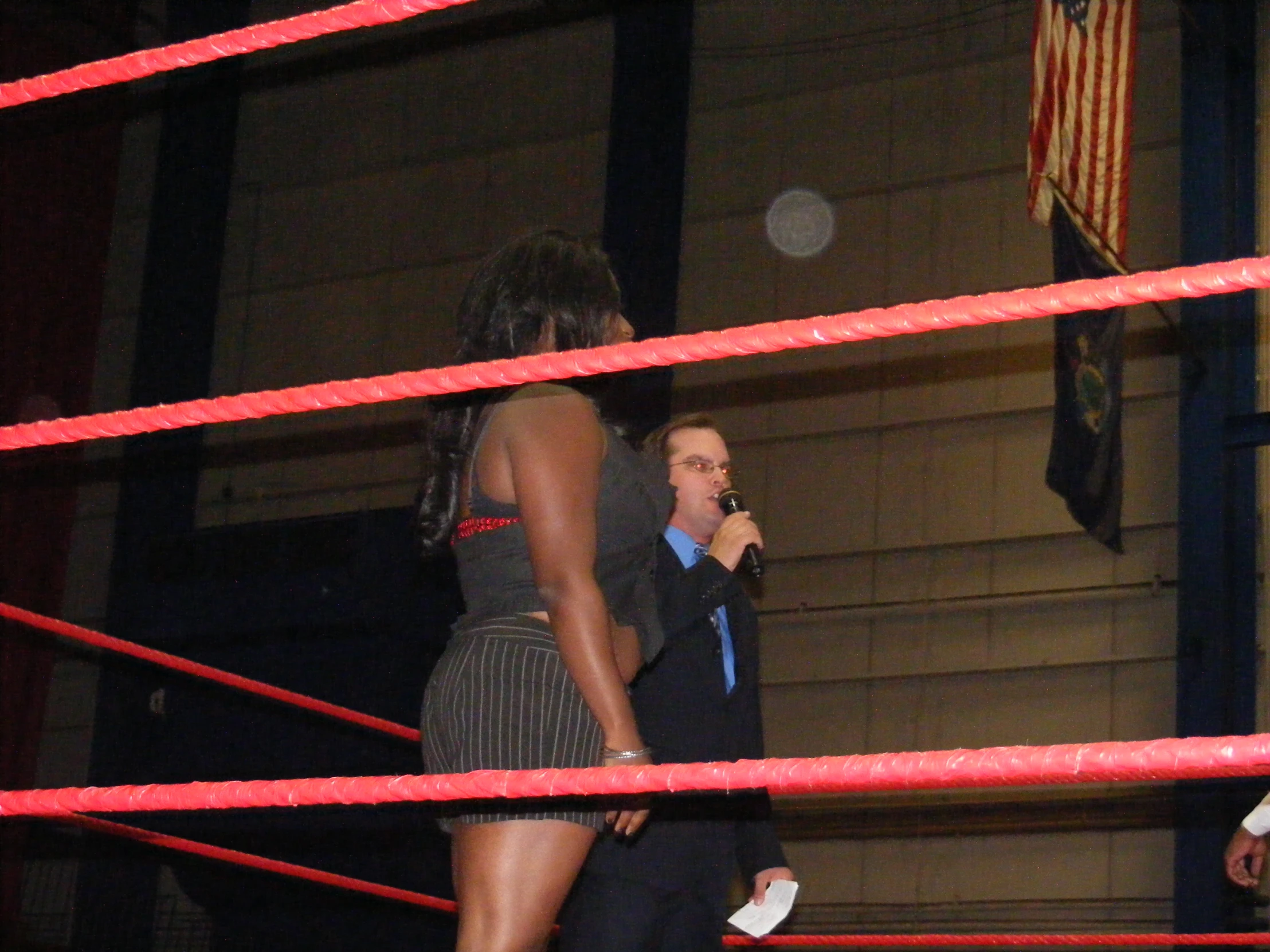 a man standing behind a red wrestling ring while a woman talks on a cell phone