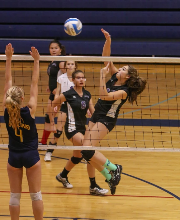 girls on opposing teams compete over volley ball