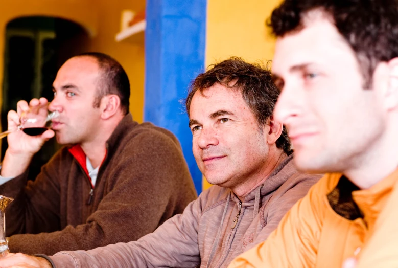 three men sitting around drinking wine together