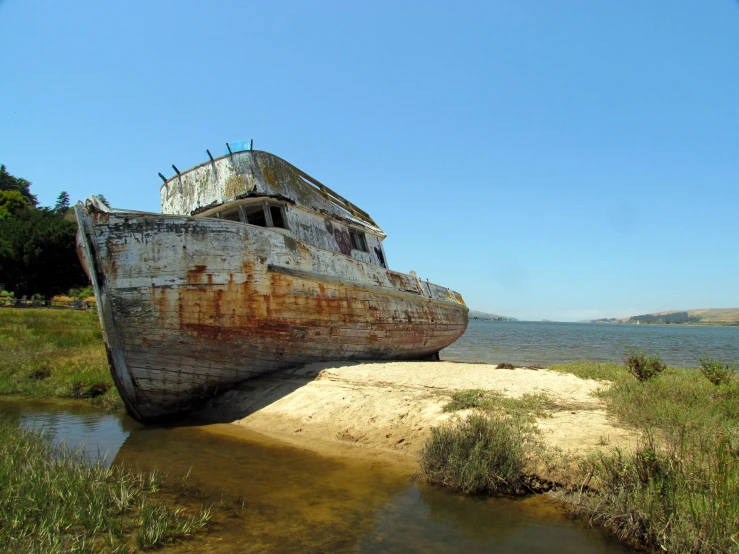 an abandoned boat sitting on a shoreline near the ocean