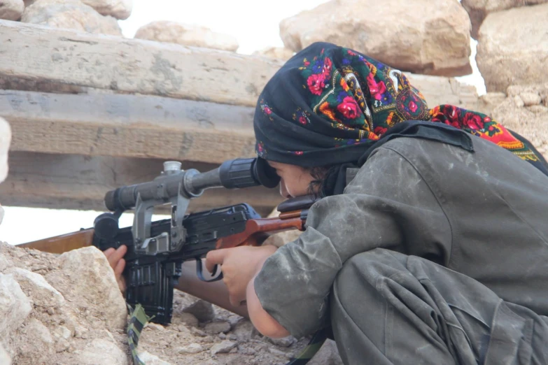 a woman sitting on the ground holding an rifle