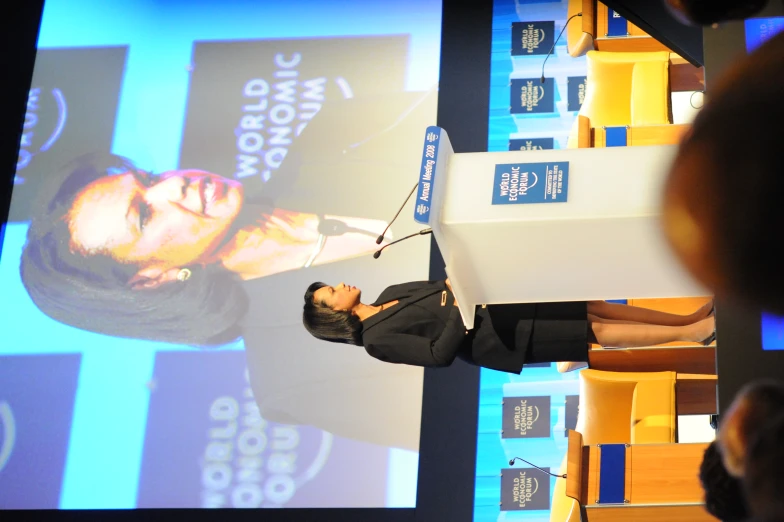 a woman standing at a podium in front of a projected wall