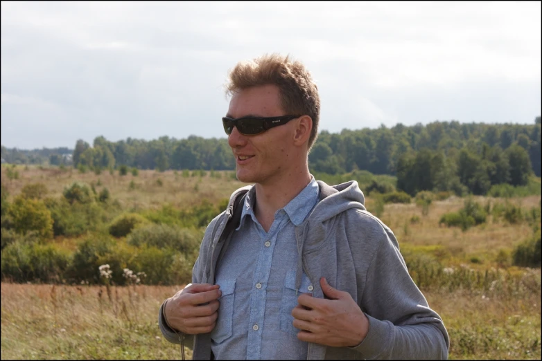 man in grey hoodie standing outdoors in grassy field