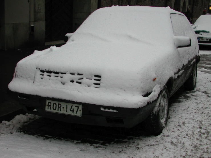 a car covered in snow is parked next to other cars