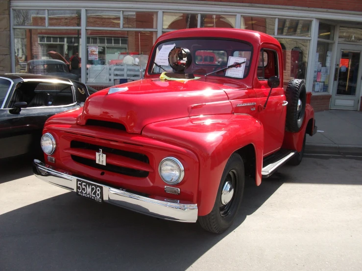 an older, red truck is parked in front of a building