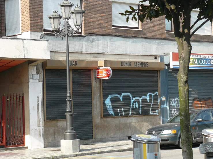 a grey streetlight next to a street with a graffiti covered store on it