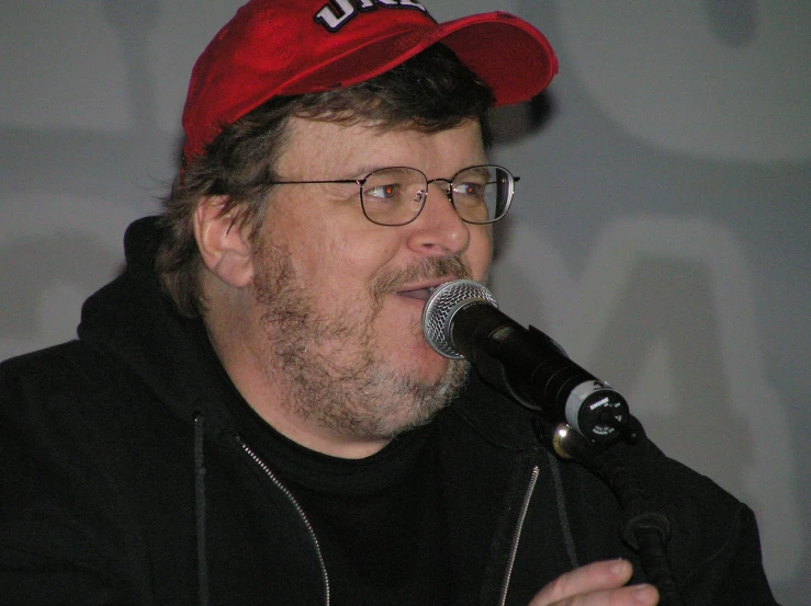 a man with glasses and a red cap is speaking into a microphone