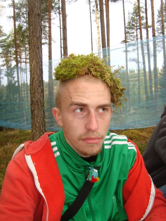 a man with green hair is sitting by a tree