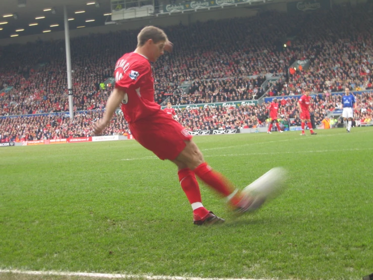 man in red shirt kicking soccer ball on green field