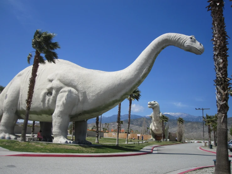 two giant dinosaurs standing next to each other near palm trees
