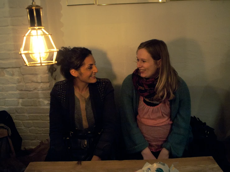 two women smiling together at a table with a lamp