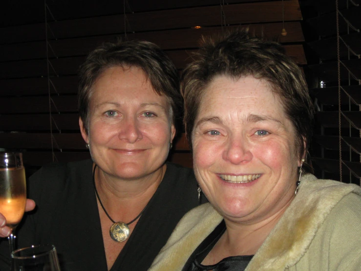 two women pose for a pograph with one holding a glass of champagne