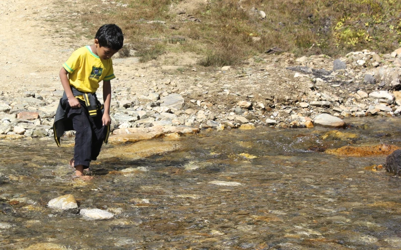 a boy in yellow shirt standing on rock next to river