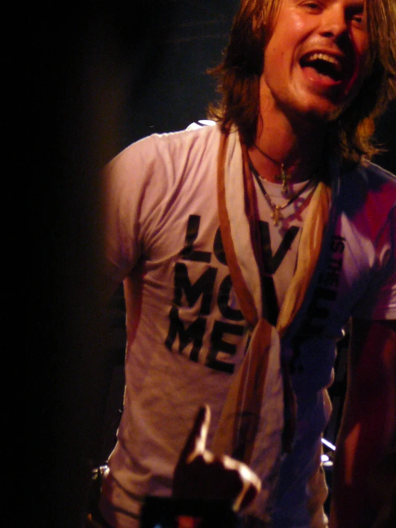 young man wearing scarf and t - shirt laughing on stage