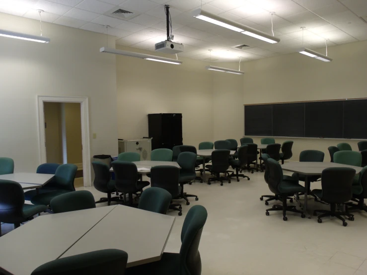 an empty classroom with blackboard and green chairs