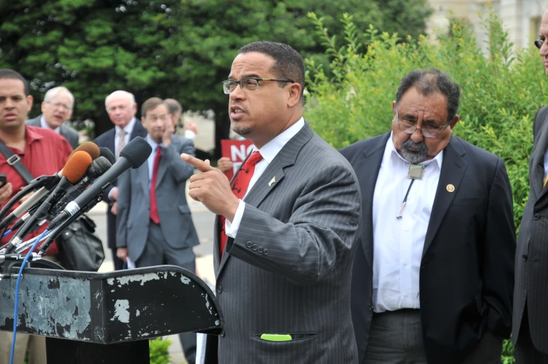 three men are speaking and standing around microphones