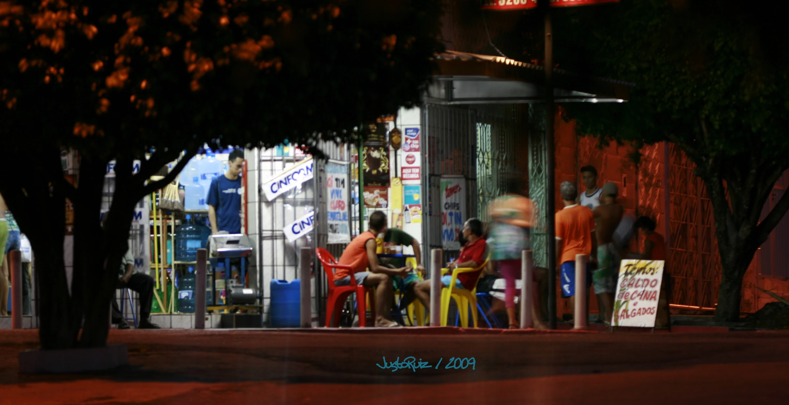 four people standing around in the dark, outside a shop