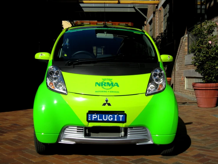 the green, modern, car is parked in front of some brick sidewalks