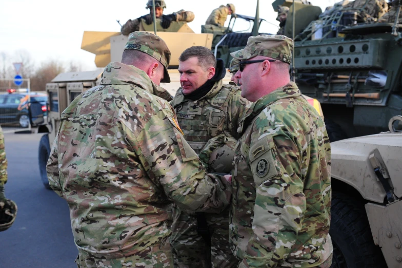 several men are talking with each other near military vehicles