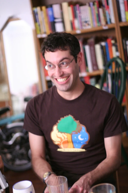 a man is smiling and sitting at a table with two glasses of water in front of him