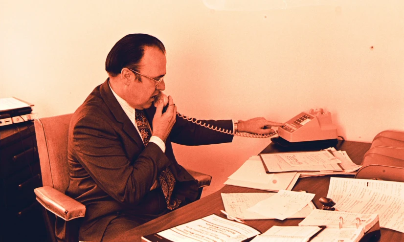 a man sitting at his office desk talking on the telephone